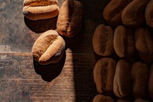Nybakade ljusa brödbullar på ett mörkt träbord, med ljus och skugga