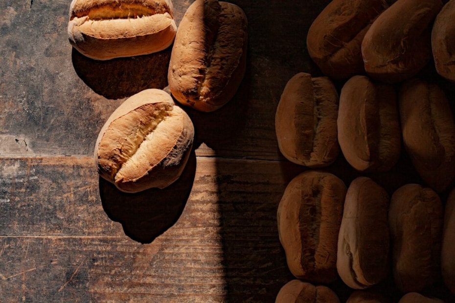 Nybakade ljusa brödbullar på ett mörkt träbord, med ljus och skugga